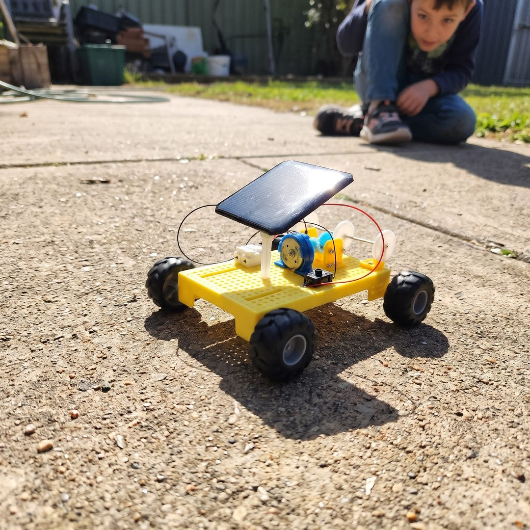 Dečak gleda svoj sklopljeni solarni auto kako vozi napolju na suncu